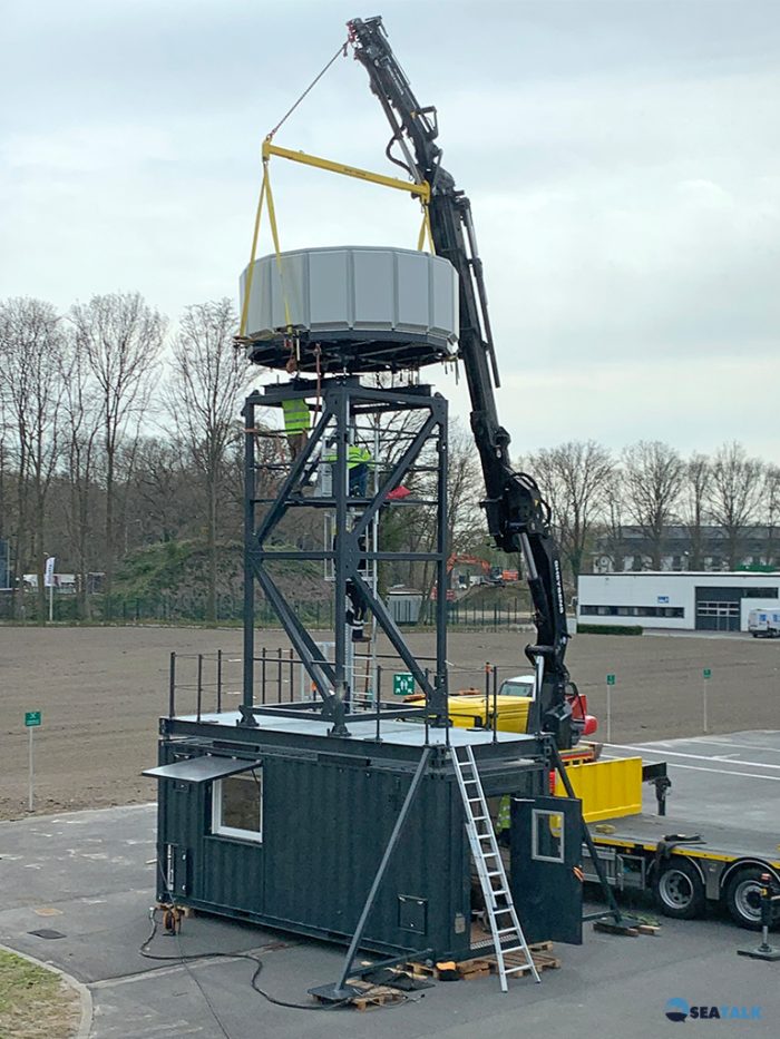 Het demonstratiemodel van de niet-roterende IFF antenne van Advionics op de bedrijfssite in Oostkamp bestaande uit een container voor de operator van de Monopulse Secondary Surveillance Radar MSSR 2000 I met daarop een zes meter hoge toren met de antenne.
